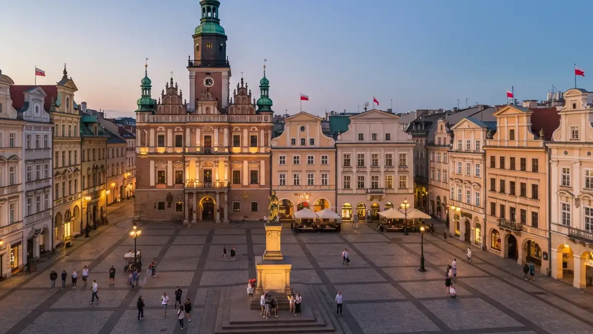 Rynek Poznański z Ratuszem wieczorem, oświetlone renesansowe budynki, turyści spacerujący po placu